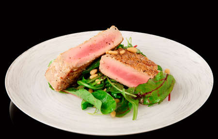 Lightly seared tuna steak and fresh salad isolated on blackの写真素材