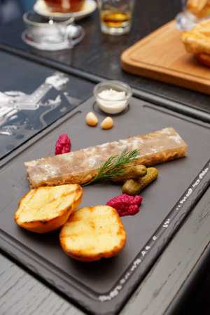 Meat aspic with baked potatoes, gherkins and horseradish on stone plateの写真素材