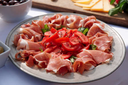 Platter with cured ham and tomatoes on tableの写真素材