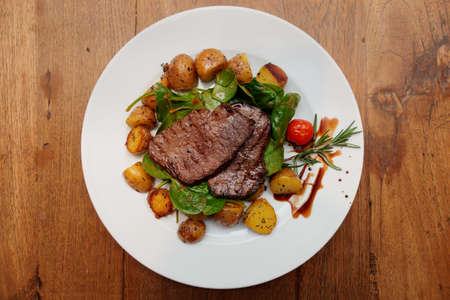 Steak with fried potatoes and spinack on wooden table の写真素材