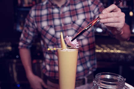 Bartender is decorating a cocktail with mango slicesの写真素材