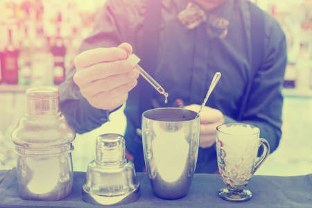 Bartender is making cocktail at bar counter, adding some bitter in the shaker, toned imageの写真素材