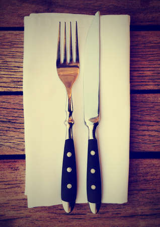Fork, knife and napkin on wooden restaurant table, toned imageの写真素材