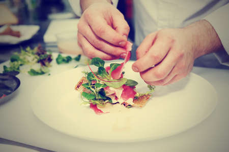 Chef is making fish appetizer on restaurant kitchen, toned imageの写真素材