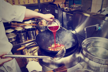 Chef is pouring sour sauce in wok at commercial kitchen, toned imageの写真素材