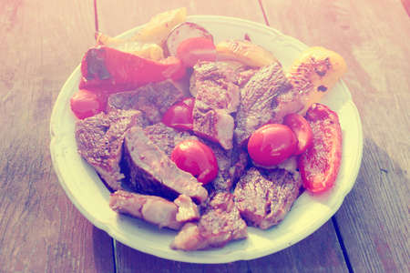 Medium rare fried steak with vegetables in plate on old wooden table, toned imageの写真素材