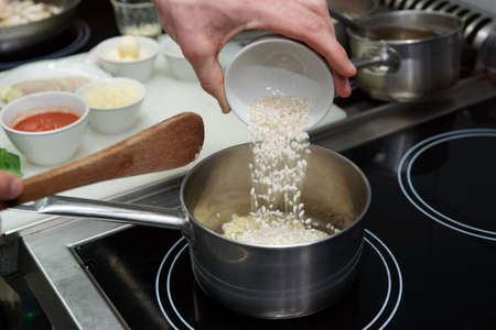 Chef is pouring rice in stewpan to cook risottoの写真素材
