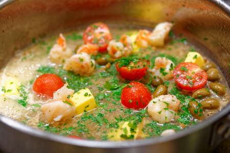 Shrimps being cooked in broth and butter wint tomatoes, capers and parsleyの写真素材