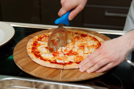 Chef is cutting pizza at commercial kitchenの写真素材