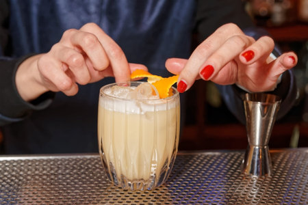 Female bartender is adding orange zest to cocktail