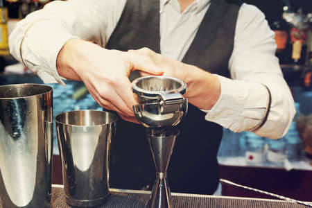 Bartender is squeezing citrus juice in jigger, toned imageの写真素材