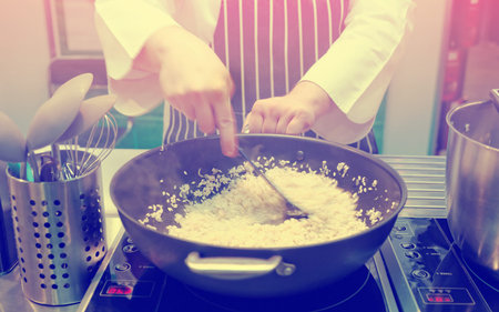 Chef is stirring risotto in a large pan, strong motion blur, toned image