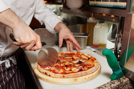 Chef is cutting pizza at commercial kitchen