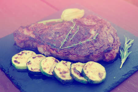 Rib eye steak with vegetables on a slate plate, toned imageの写真素材