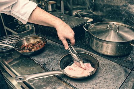 Chef is frying chicken fillet at restaurant kitchen, toned imageの写真素材