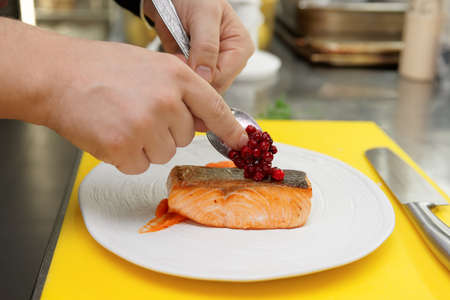 Chef is topping fried salmon steak with berry sauce at professional kitchenの写真素材