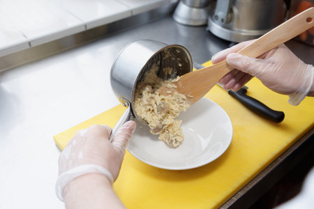 Chef is putting mushroom risotto in plate, commercial kitchen work