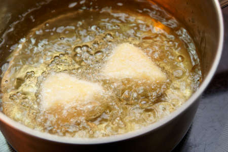 Deep fryer with pieces of breaded camembert cheese cooking in boiling oil, close-upの写真素材