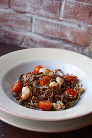Rye pasta with capers and prawns in white porcelain plate against brick wall