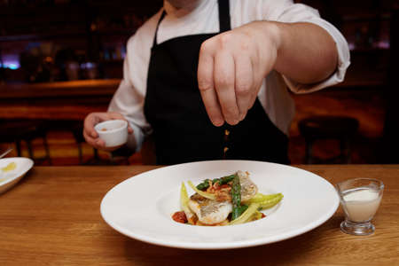 Chef is adding fried onion chips to a fish dishの写真素材