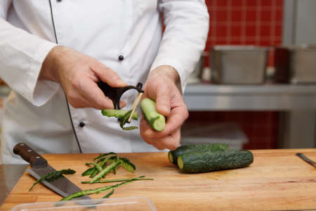 Chef is peeling cucumbers in restaurant kitchen, copy spaceの写真素材