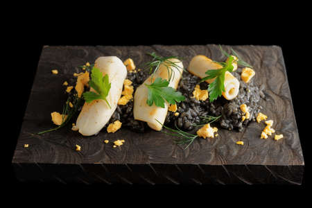Black isotto with squid ink and seared calamary on wooden board, isolated on blackの写真素材