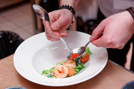 Chef is decorating prawn appetizer with salmon roe, commercial kitchen, slight motion blur, toned...