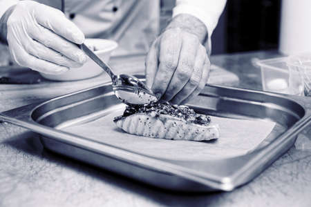 Chef is putting herbal sauce on grilled salmon steak to make a savory crust, toned imageの写真素材
