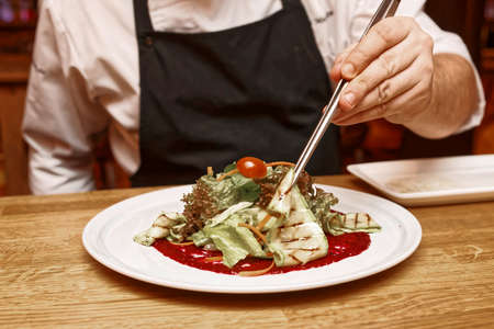 Chef is serving vegetable appetizer with pincers on white porcelain plate, toned imageの写真素材