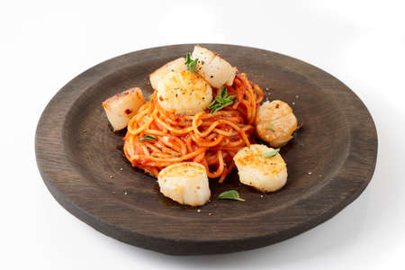 Pasta with fried scallops, oregano and tomato sauce on black wooden plate isolated on white backgroundの写真素材