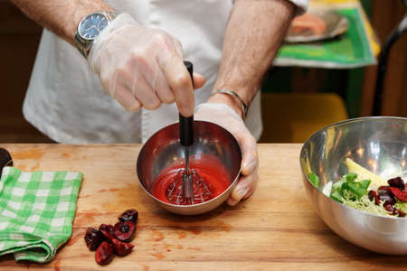 Professional cook is making salad dressing of red cherry berries, oil and vinegar with whiskerの写真素材