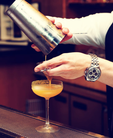 Bartender is pouring cocktail from shaker into a glass, toned image