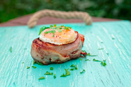 Grilled tenderloin steak wrapped in bacon with egg and chopped herbsの写真素材