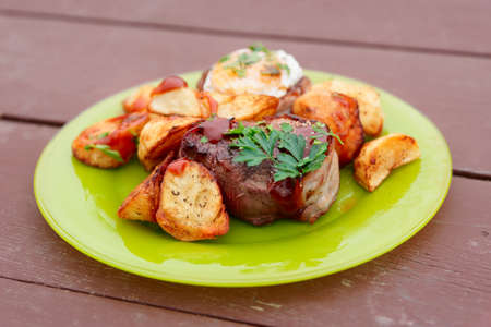 Tenderloin steaks with fried eggs and potatoes in green glass plateの写真素材