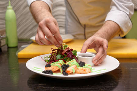 Chef is serving crab cakes with salad mix, gravy, seaweed caviar and wasabi sauceの写真素材