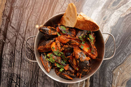 Mussels cooked with hot Italian arrabiata sauce and served in metal potの写真素材