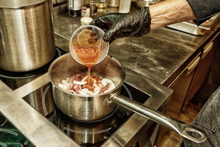 Gloved chef is adding strained tomatoes to a dish, professional kitchen, toned photo, HDR styleの写真素材