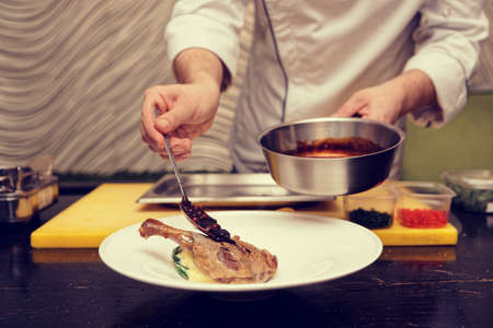 Chef is pouring berry sauce over dried duck leg, toned, noise addedの写真素材