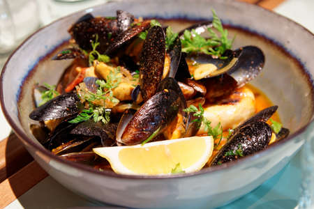Mussels in a deep clay bowl with turmeric sauce and lemon の写真素材