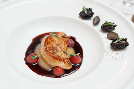 Fried duck liver with wine sauce and berries in white china plateの写真素材