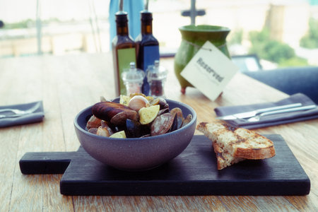 Shelfish sautee on dark cutting board on reserved restaurant table, toned image