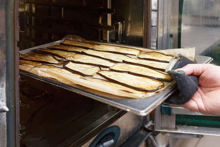 Chef is putting baked egg-plants out of professional ovenの写真素材