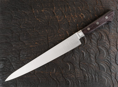 Long chef's knife on black wooden cutting board shot from above