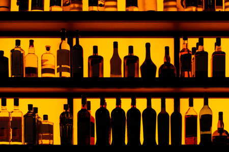 Rows of bottles sitting on shelf in a bar, yellow backlightの写真素材