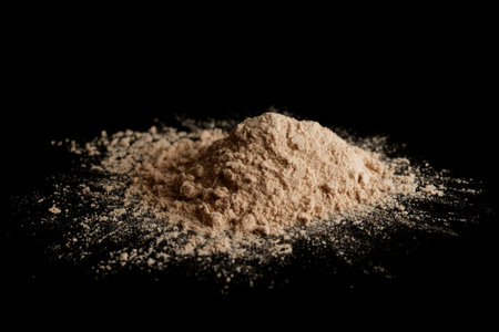Spilled brown powder looking like unrefined heroin isolated on black background