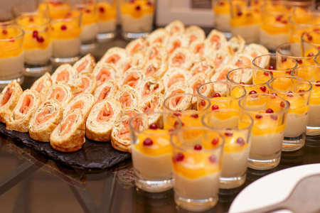 Pancakes rolls with salmon and glasses of panna cotta on banquet tableの写真素材