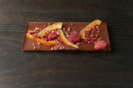 Chocolate bar with candied orange peel and raspberry on dark wood cutting boardの写真素材