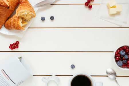 Tasty breakfast with coffee, berries, croissant on the white wooden table with copy space, top view