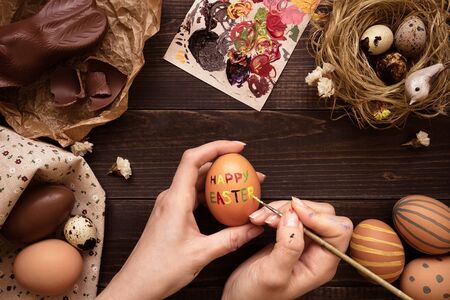 Happy easter. Female hands painting easter egg on the wooden table.の写真素材