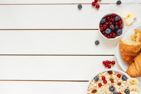 Healthy breakfast with oat flakes, berries, croissants on the white wooden table with copy space, top view.の写真素材